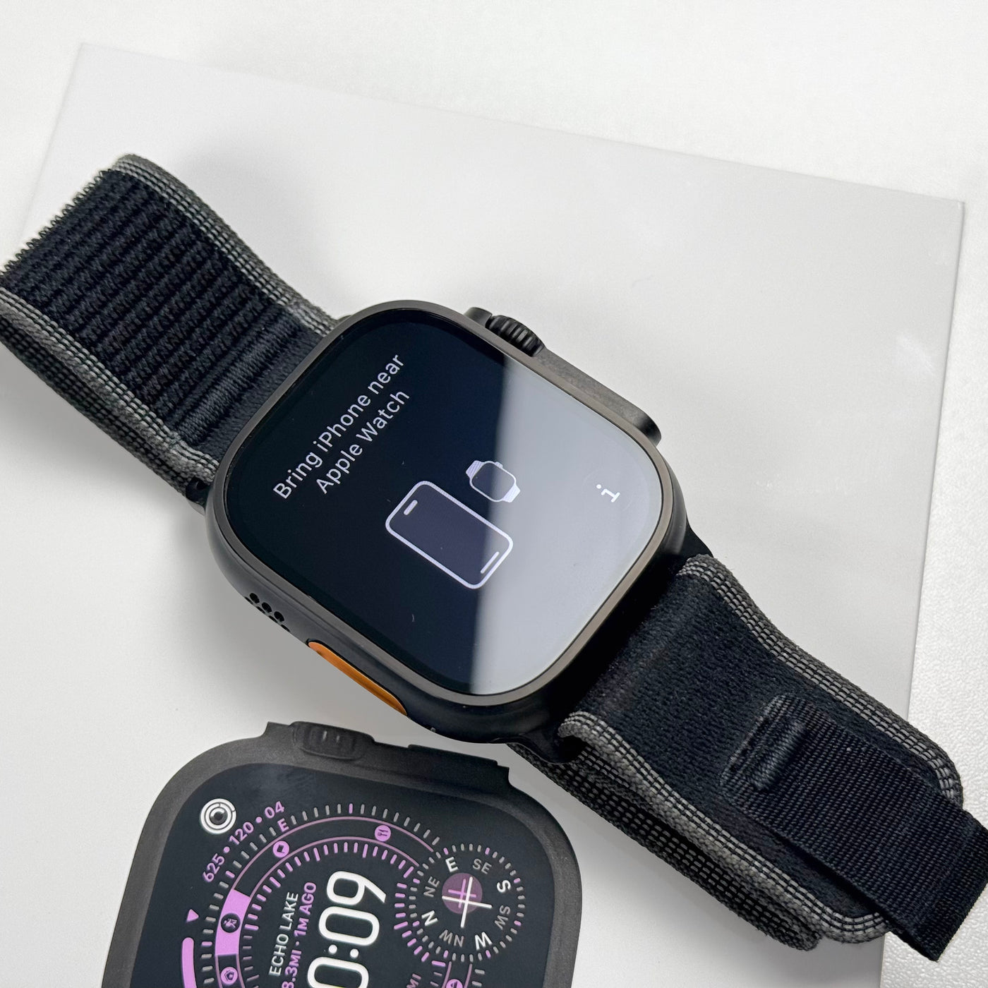 Pre-owned Apple Watch Ultra 3 Black Titanium with Trail Loop, screen on, beside box - MacShack