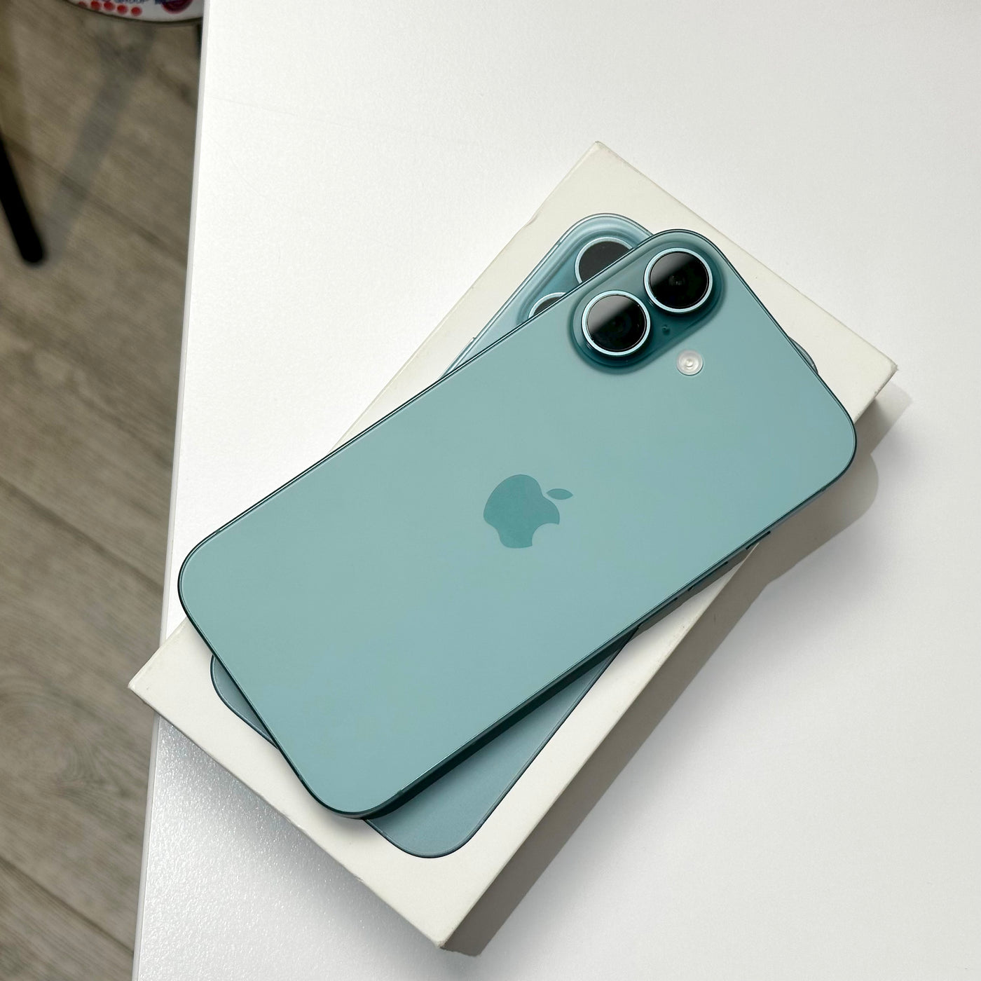 Back of the pre-owned iPhone 16 in Teal showing the dual camera, resting on its original box - Mac Shack