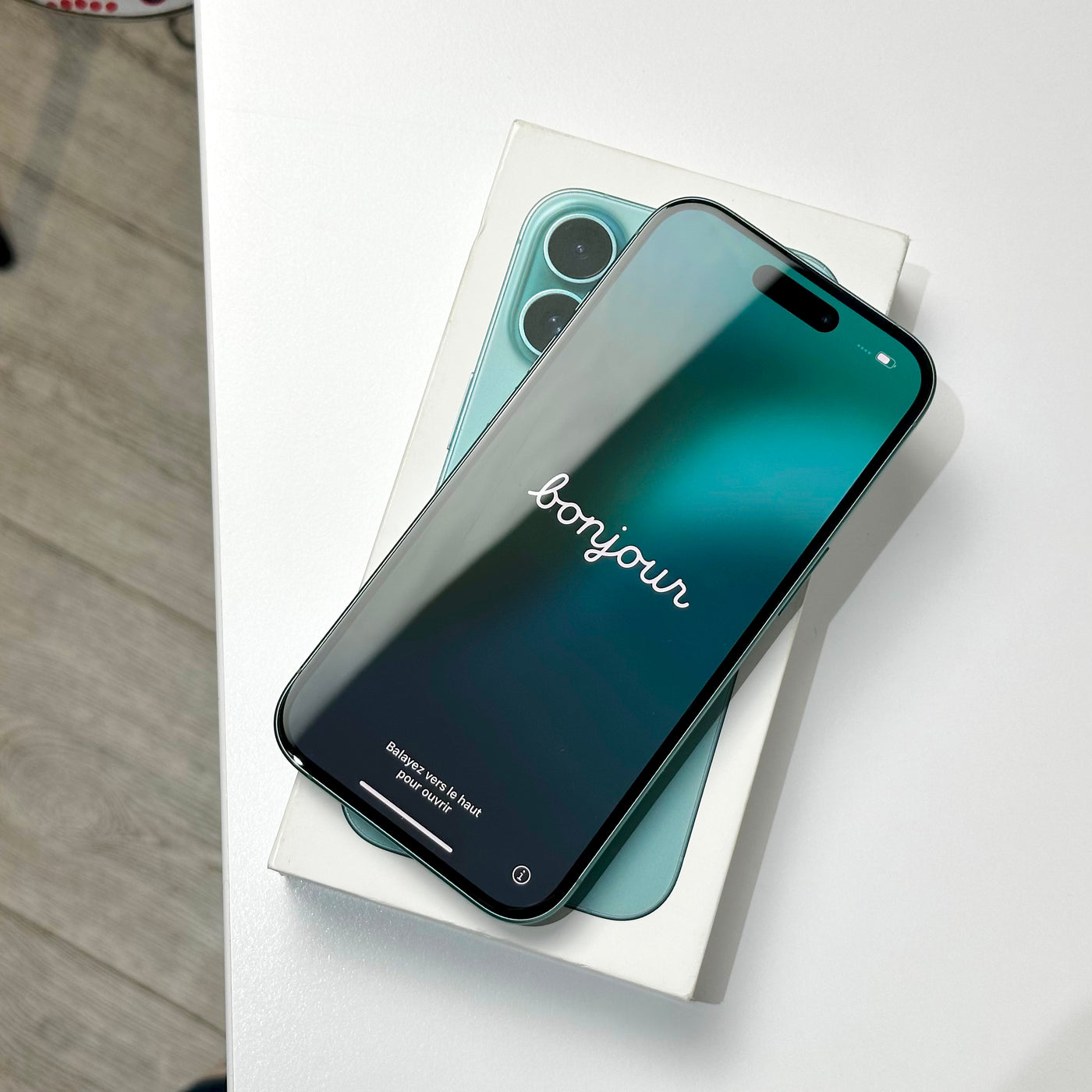Pre-owned iPhone 16 in Teal with the screen on, resting on its original box - Mac Shack