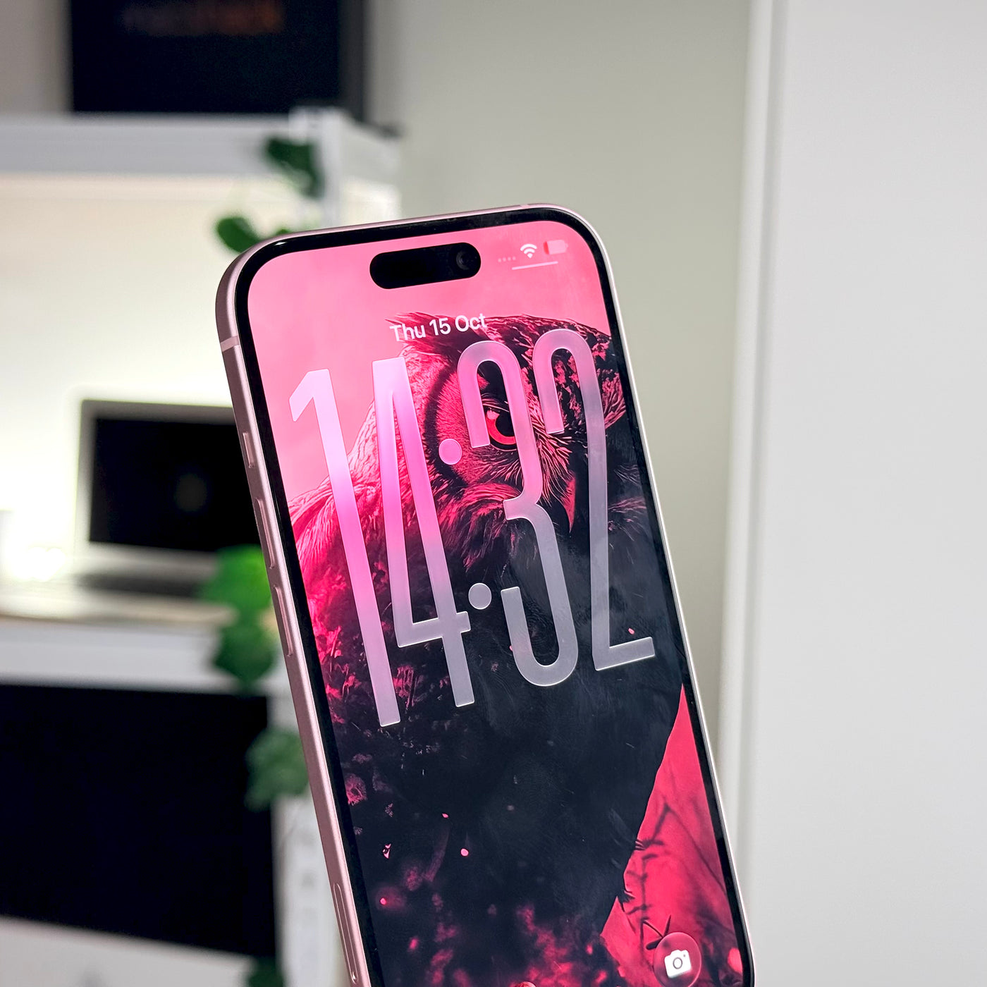 Pre-owned pink iPhone 15 standing upright, lock screen on