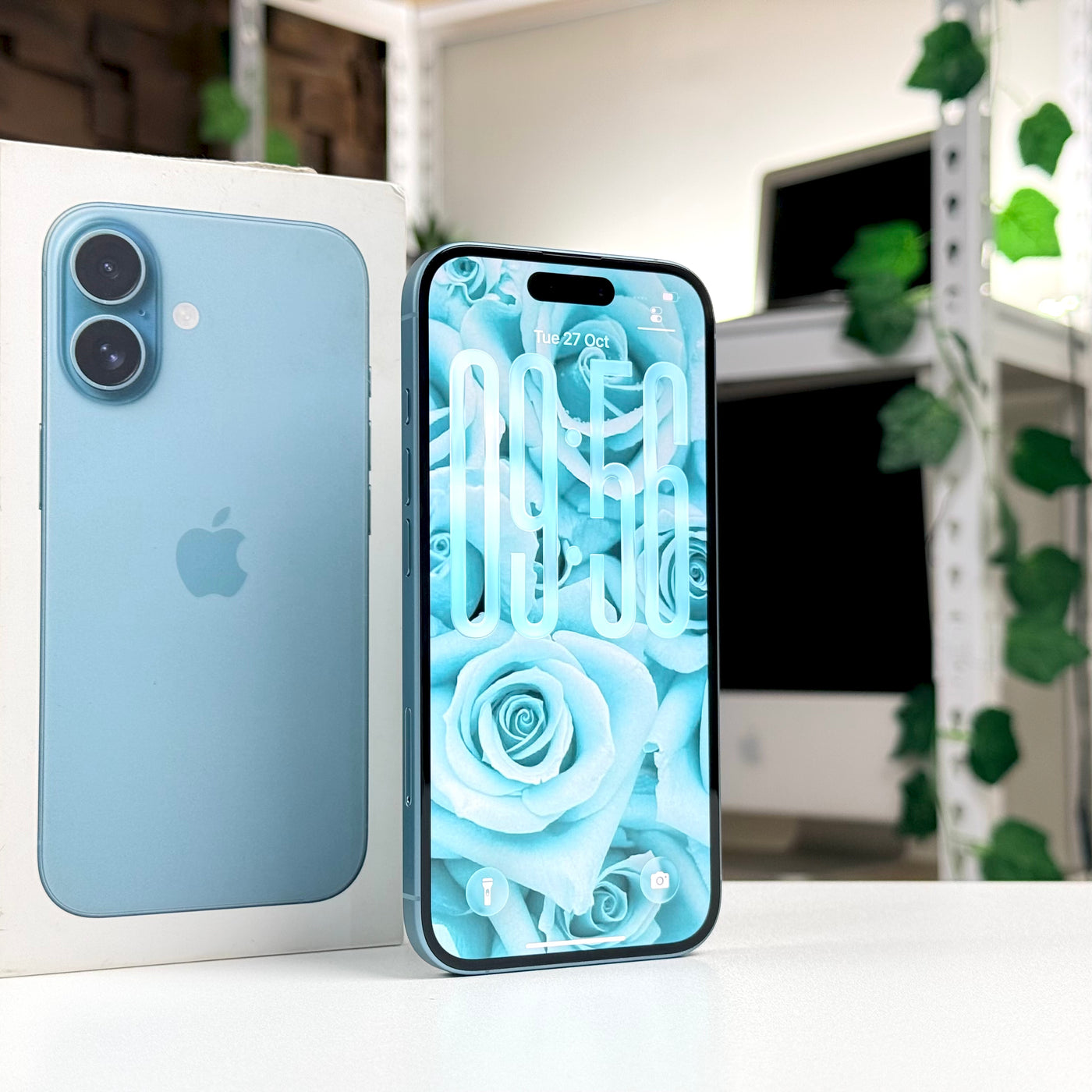 Pre-owned iPhone 16 Teal standing upright, screen on, beside original box - MacShack