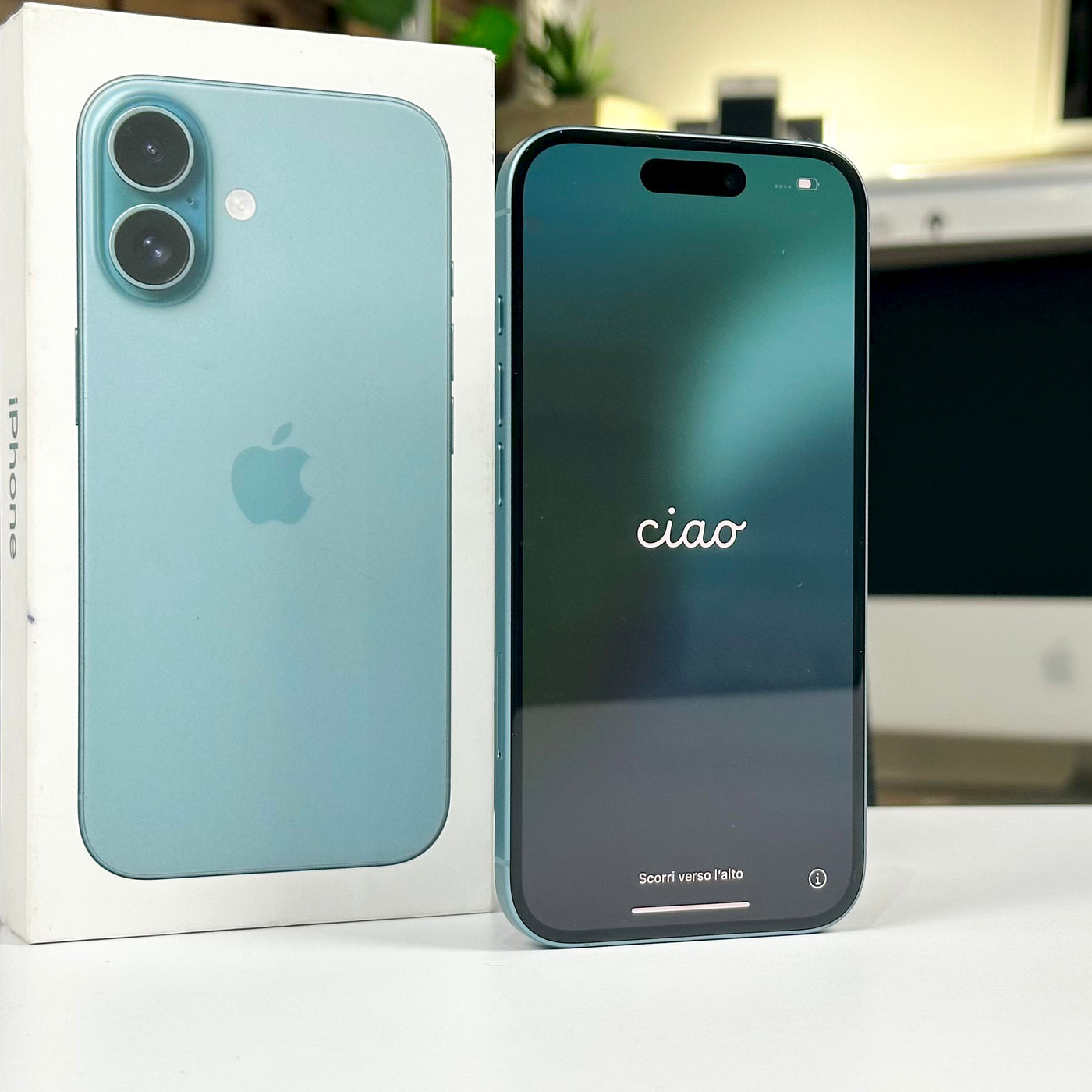 Pre-owned iPhone 16 in Teal with the screen on, standing beside its original box - Mac Shack